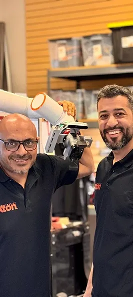 Two Axton engineers smiling beside a cobot fitted with a gripper
