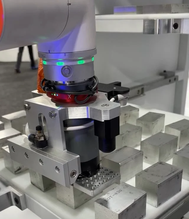 An Axton robotic gripper picking a machined block from a tray.